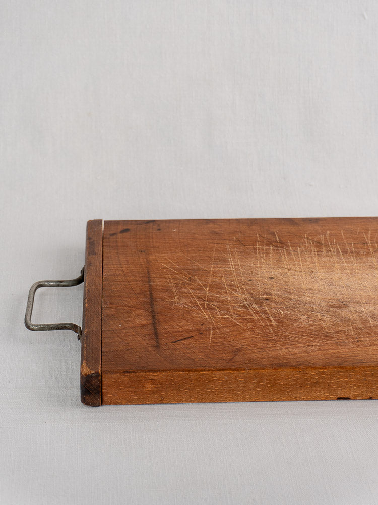 Antique French wood cutting board with hand-forged iron handle and age-worn scratches on a light gray surface.