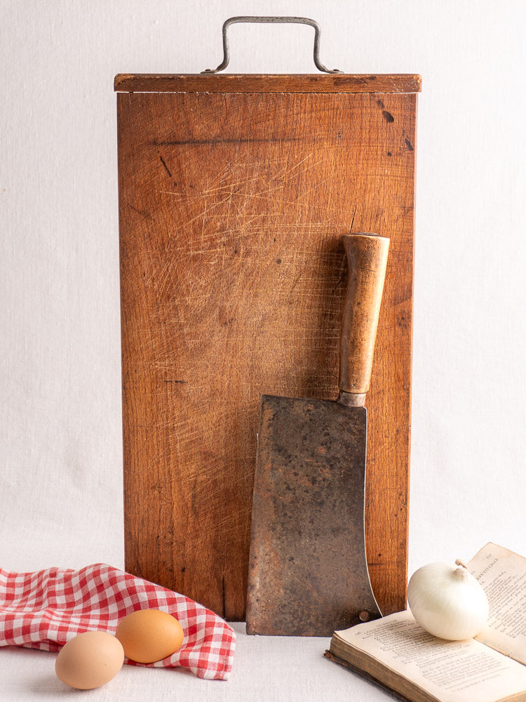 Antique French wood cutting board with iron handle, c.1890–1920, shown upright beside vintage kitchen accessories.