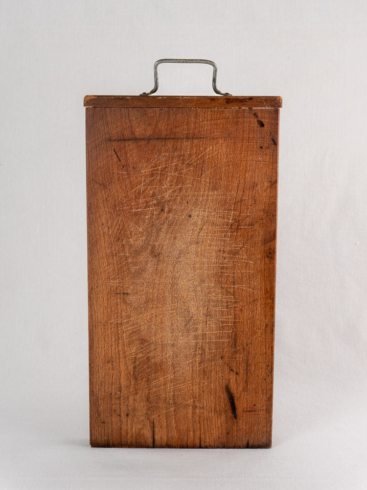 Antique French wooden cutting board with hand-forged iron handle, upright on white background, showing age-worn scratches.