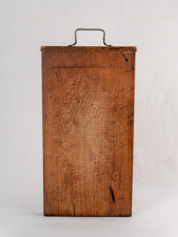 Antique French wooden cutting board with hand-forged iron handle, upright on white background, showing age-worn scratches.