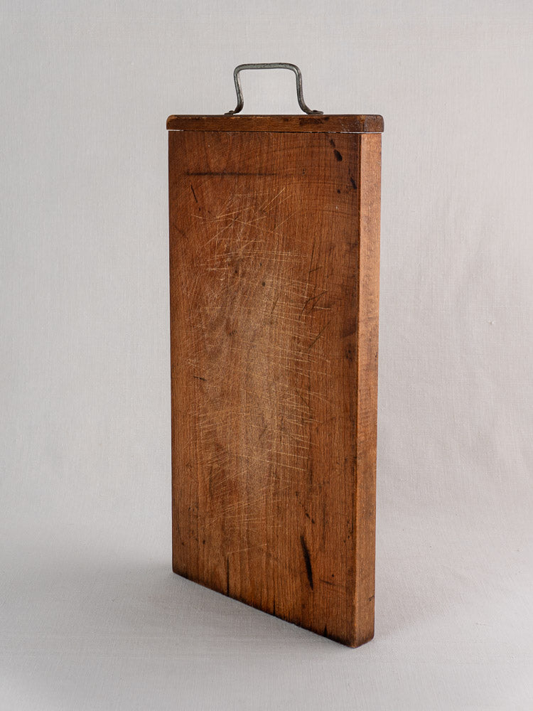 Antique French cutting board circa 1890–1920 with hand-forged iron handle, upright on a plain background.