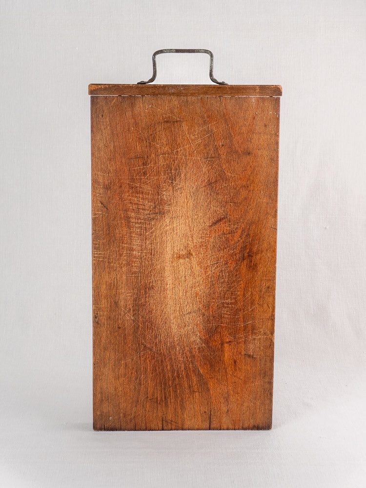 Antique French wooden cutting board with iron handle, circa 1890–1920, upright on a plain light background.