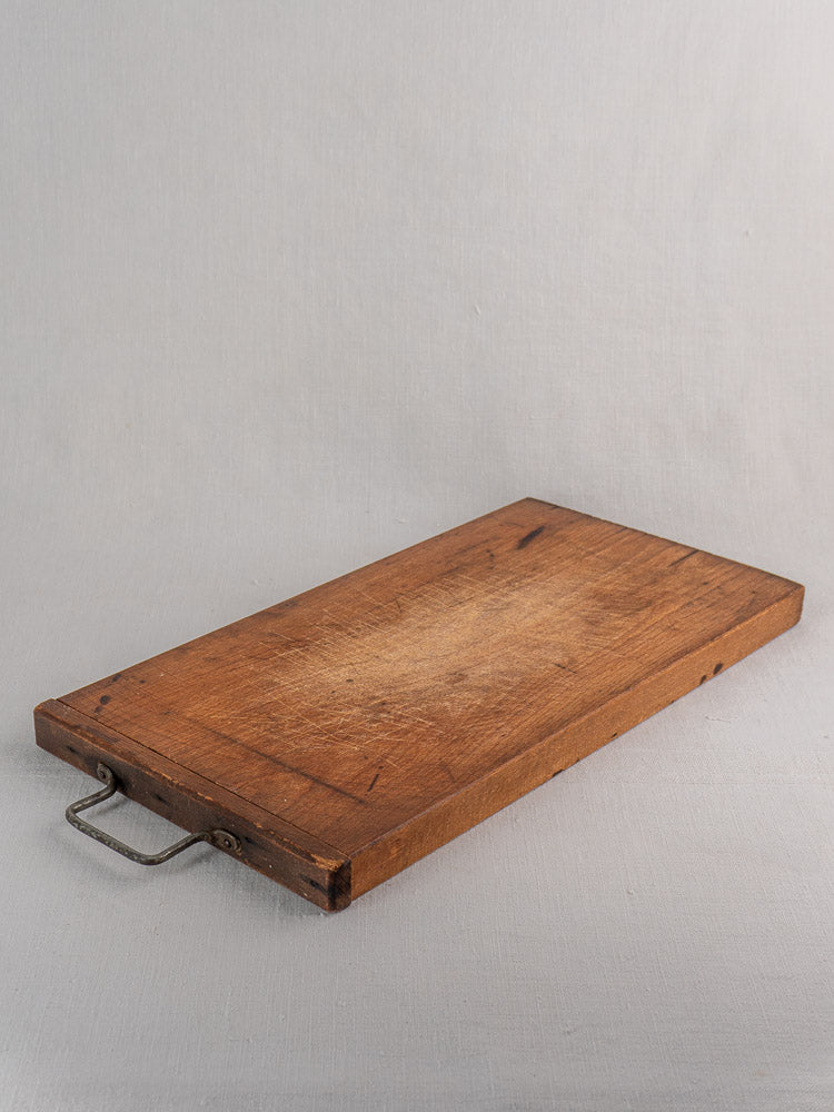 Antique French wooden cutting board with hand-forged iron handle and worn patina, on a light gray surface.