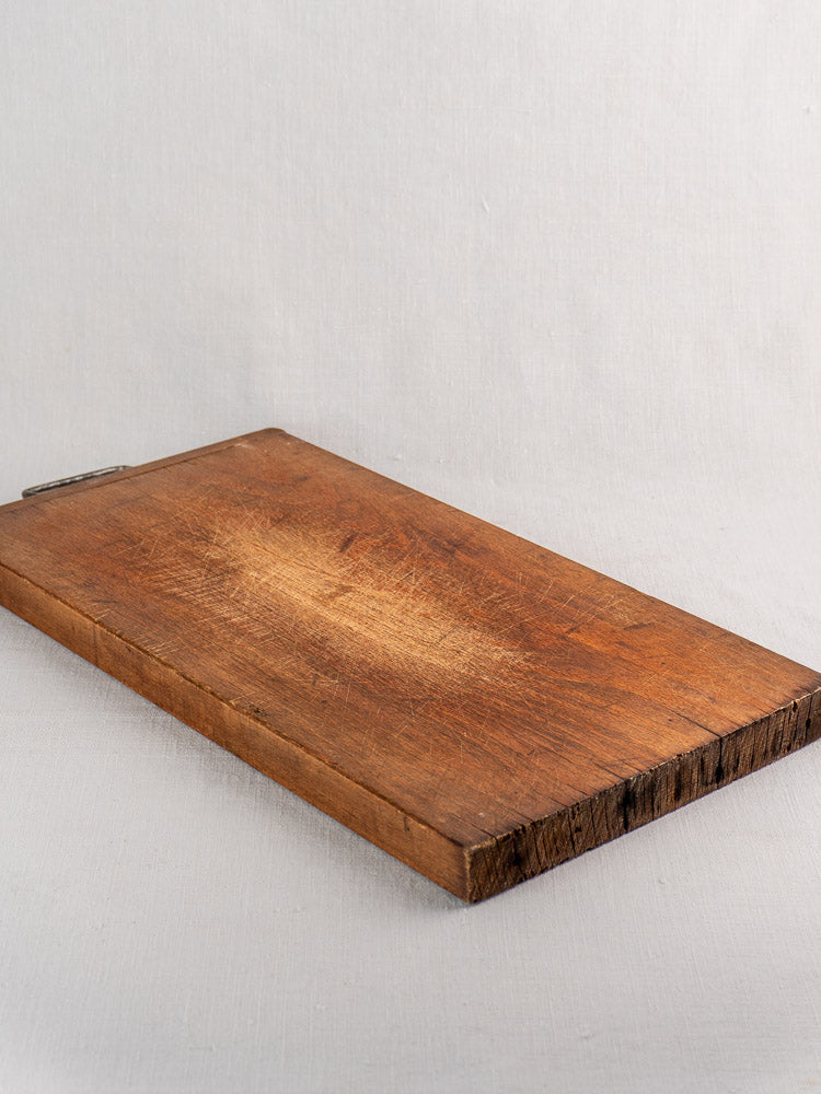 Antique French wooden cutting board with iron handle, rustic rough edges, and visible scratch marks circa 1890–1920.