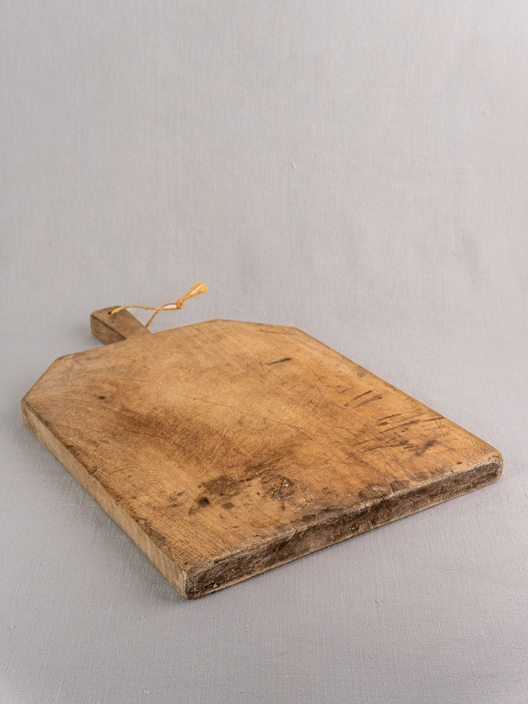 Antique French bread board, hand carved beech in provincial farmhouse style, angled on light gray surface.