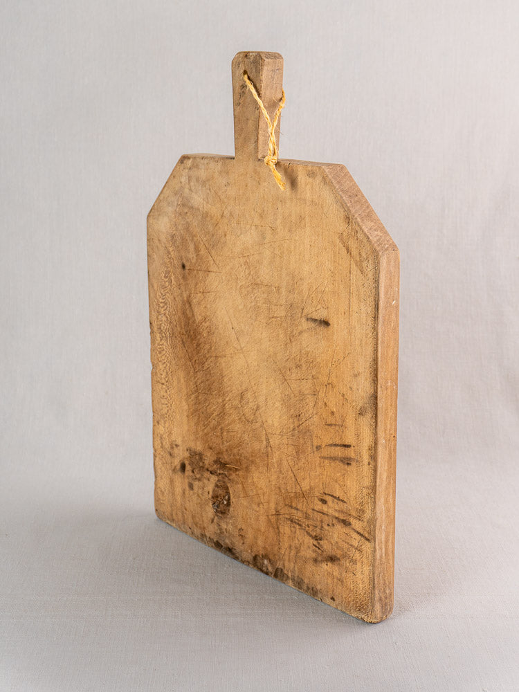 Antique French hand-carved beech bread board with handle, aged patina and yellow hanging string.