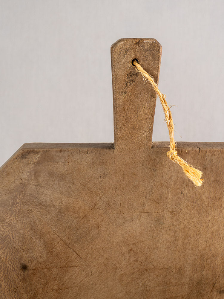 Antique French beech bread board, hand carved with handle and rustic twine, visible grain against light background.