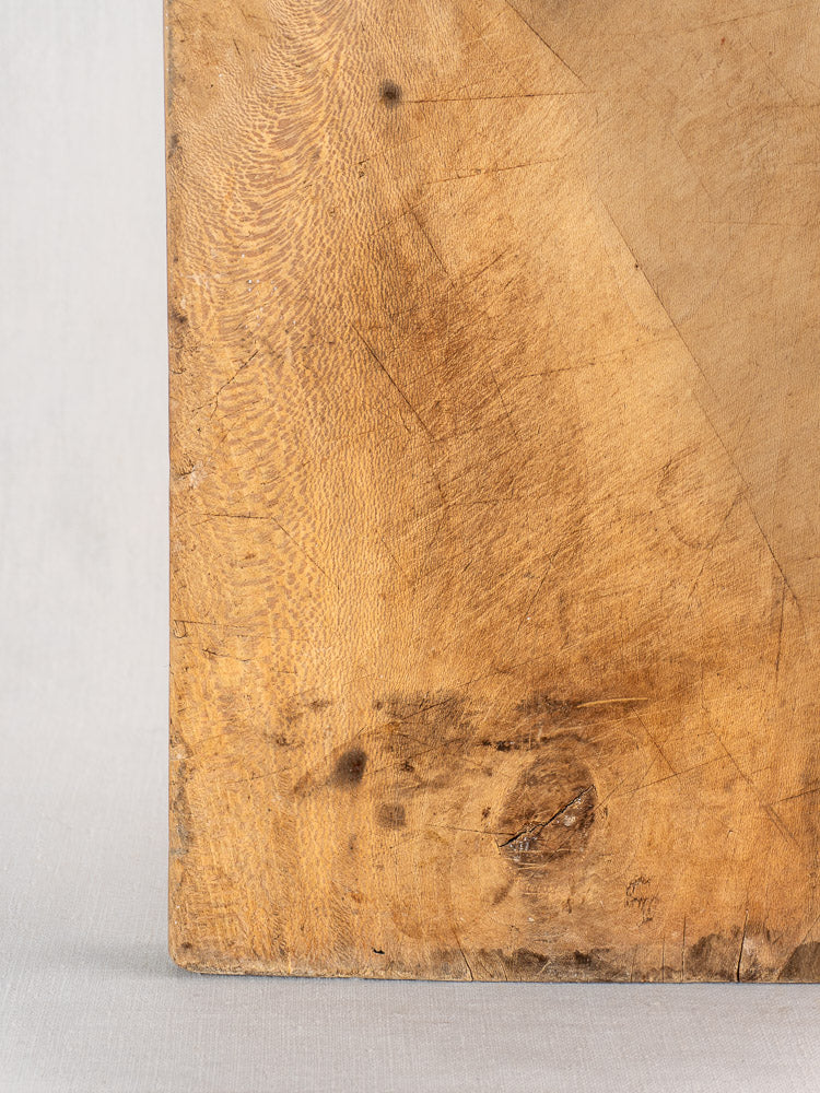 Antique French bread board in hand-carved beech, worn and scratched with dark stains, set against a light gray background.