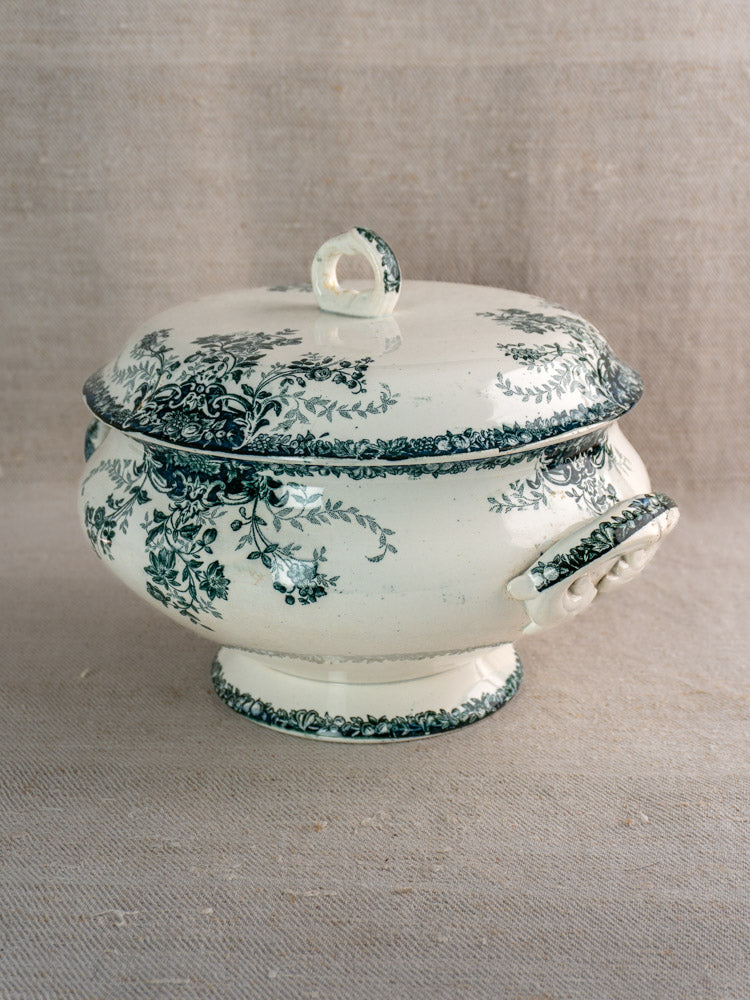 Antique French Saint-Amand faience soupière with fruit pattern and lid on neutral fabric background.