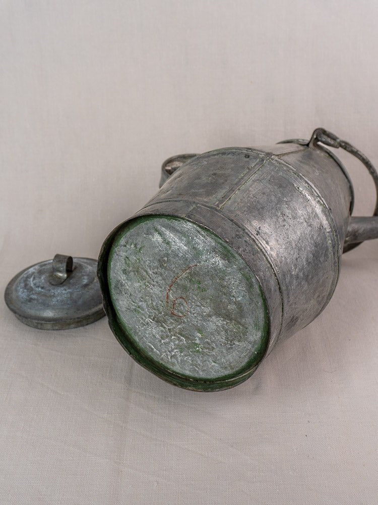 Antique French zinc watering can, milk can shape, early 20th century, lid off, on light fabric background.