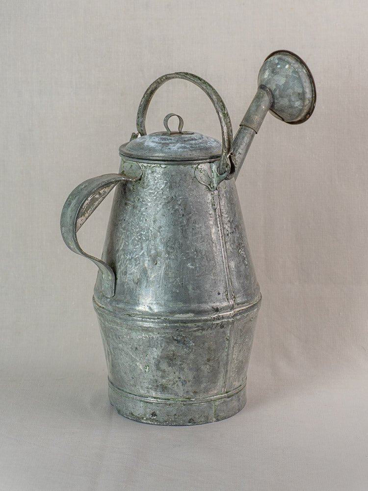 Antique French zinc watering can with side handle, hinged lid, and long spout on a light background. Early 20th century.