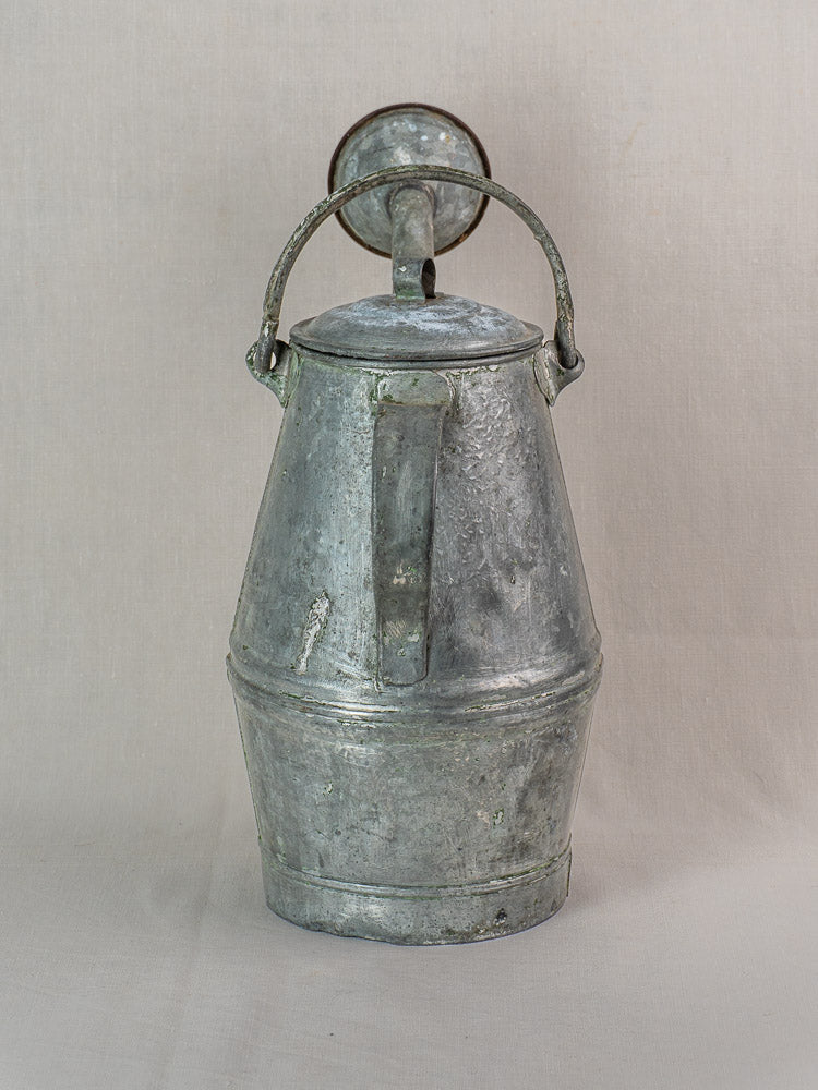 Antique French zinc watering can in milk can shape, early 20th century, upright on light beige background.