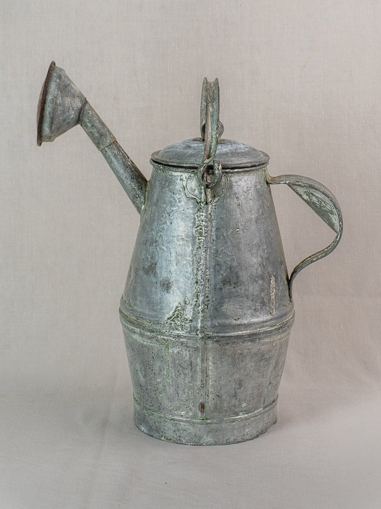 Antique French zinc watering can in milk can shape with large handle and long spout on a light background.