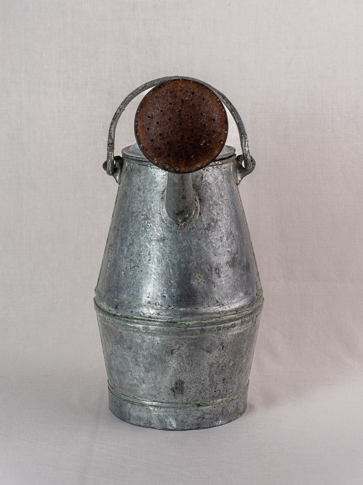 Antique French zinc watering can with rounded handle and aged spout, milk can shape on neutral background.