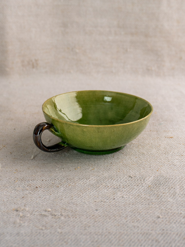 Set of six vintage French teacups with Dieulefit green glaze, dark brown handles, on textured beige fabric.