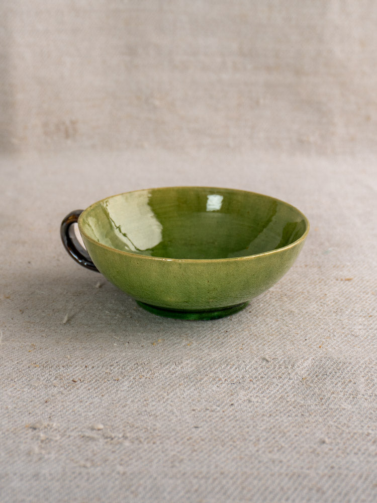 Set of six vintage Dieulefit French green glazed teacups with dark handles on beige textured fabric in soft natural light.