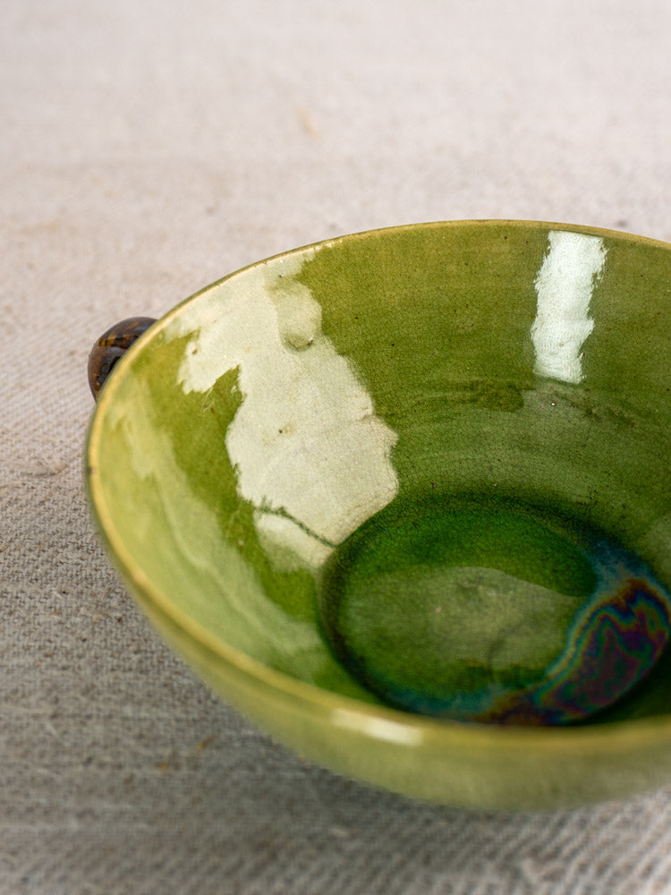 Dieulefit Green Glaze teacup with glossy green finish and small handle on textured beige fabric.