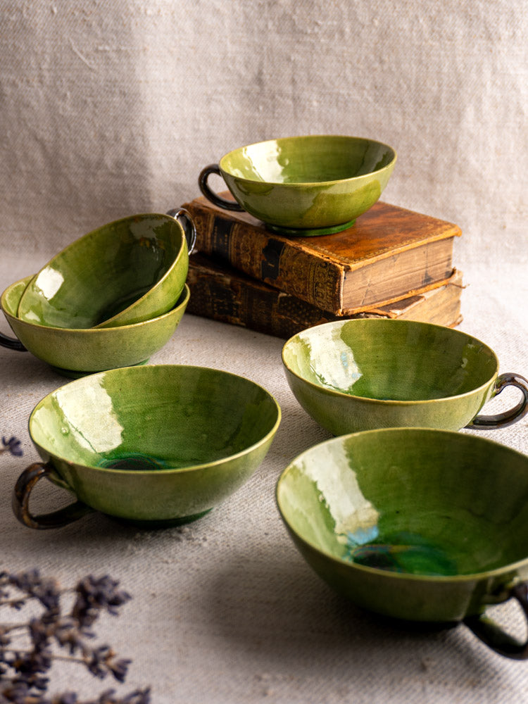 Set of six Dieulefit green glazed vintage French teacups with handles, arranged near stacked old books and dried flowers.