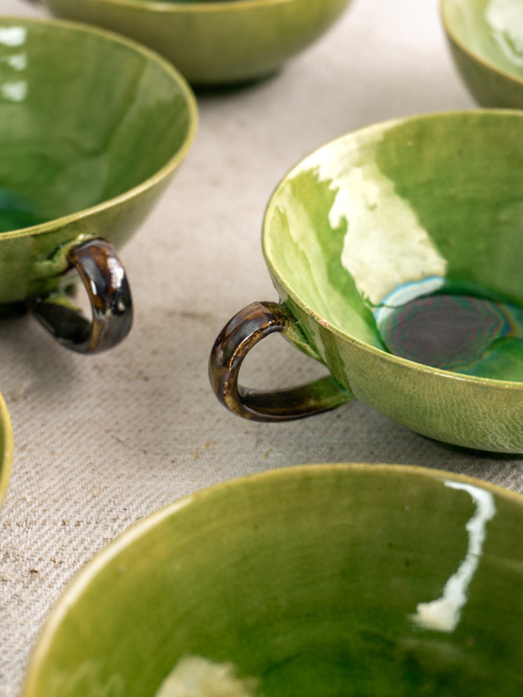 Set of six vintage French teacups in Dieulefit green glaze with unique finishes on a textured beige surface.