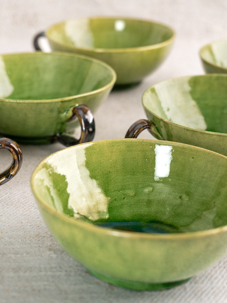 Set of six vintage French Dieulefit teacups with glossy green and cream glaze on textured surface.