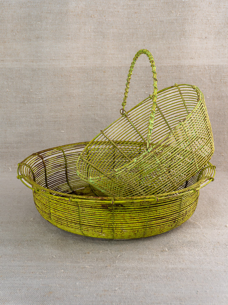 Pair of green antique French wire baskets, one nestled inside the other on a neutral surface.