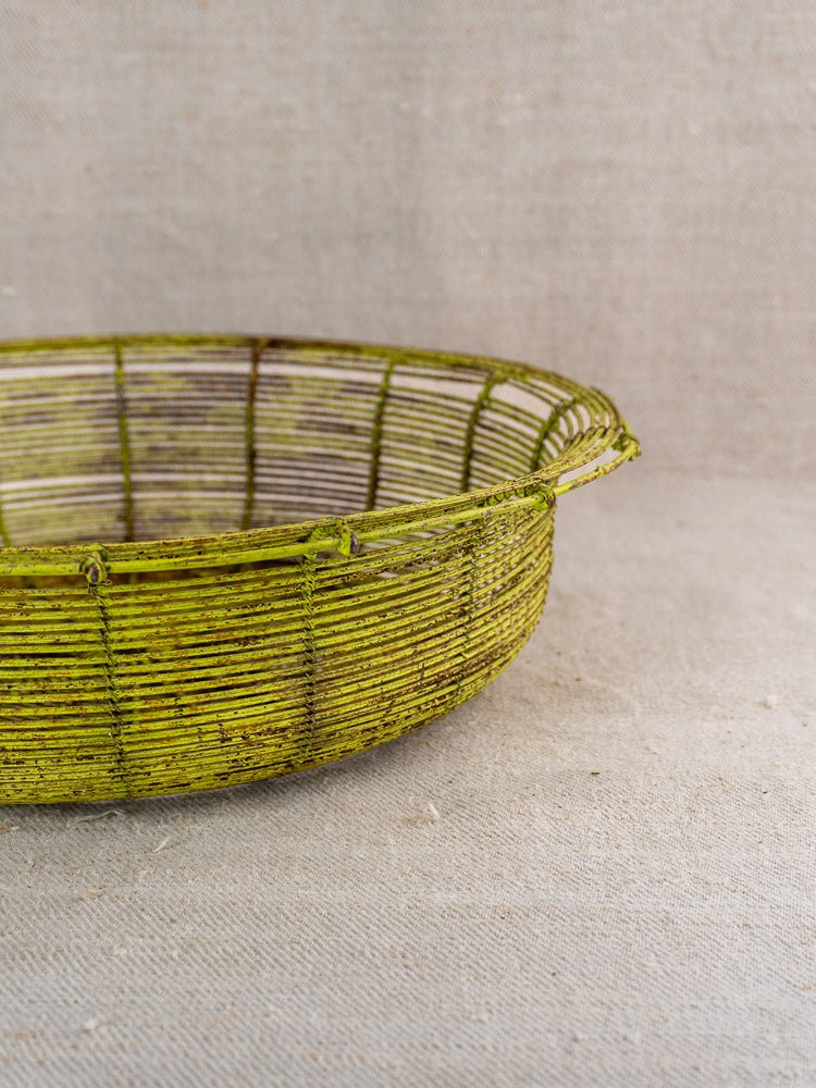 Antique French wire basket, circa 1900, vintage green, on neutral textured fabric against plain backdrop.
