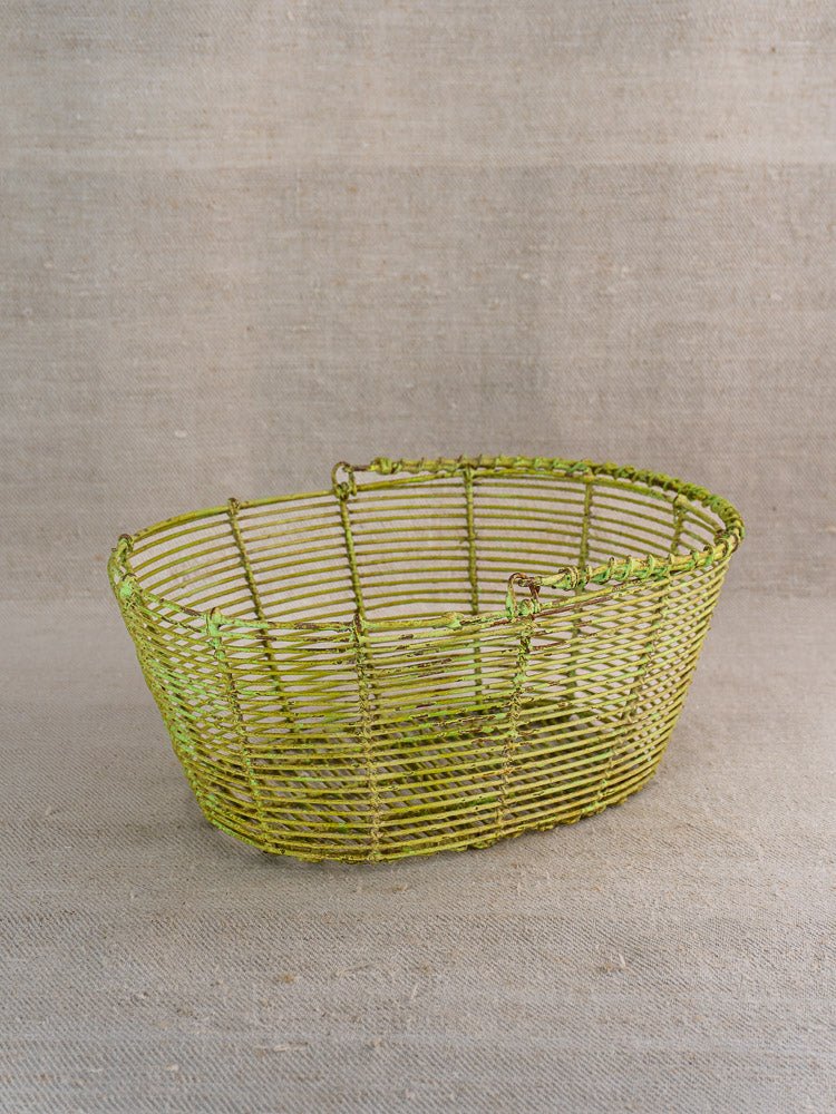Antique French green painted wire basket, circa 1900, on beige textured fabric background.