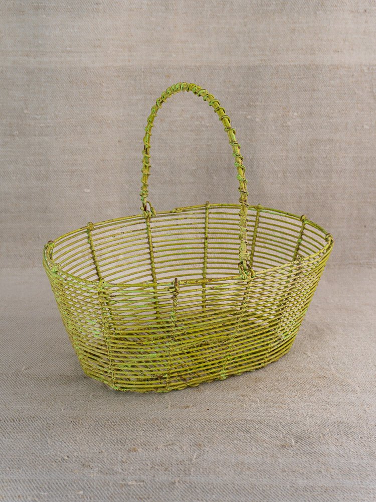 Antique French green painted wire basket, circa 1900, on textured beige fabric background.
