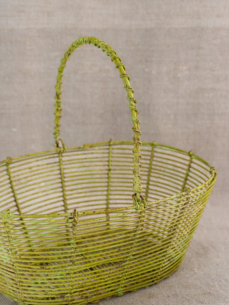 Antique French green painted wire basket, circa 1900, on textured beige fabric background.