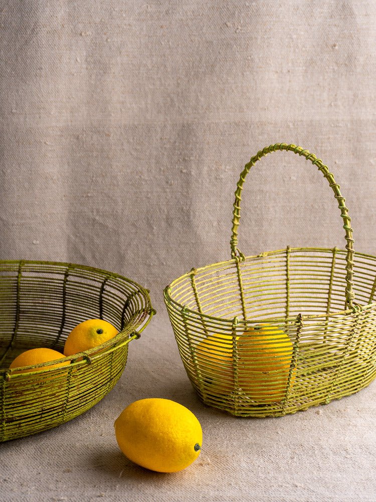 Pair of antique French green-painted wire baskets, circa 1900, holding bright lemons on beige fabric.