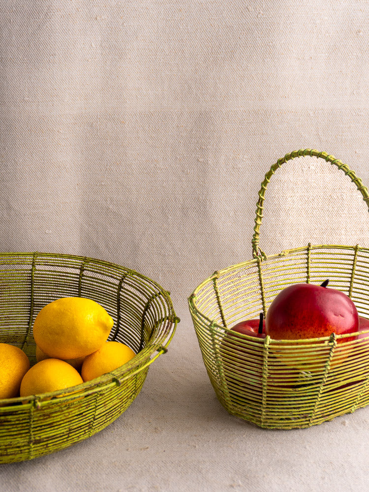 Pair of green antique French wire baskets, one nestled inside the other on a neutral surface.