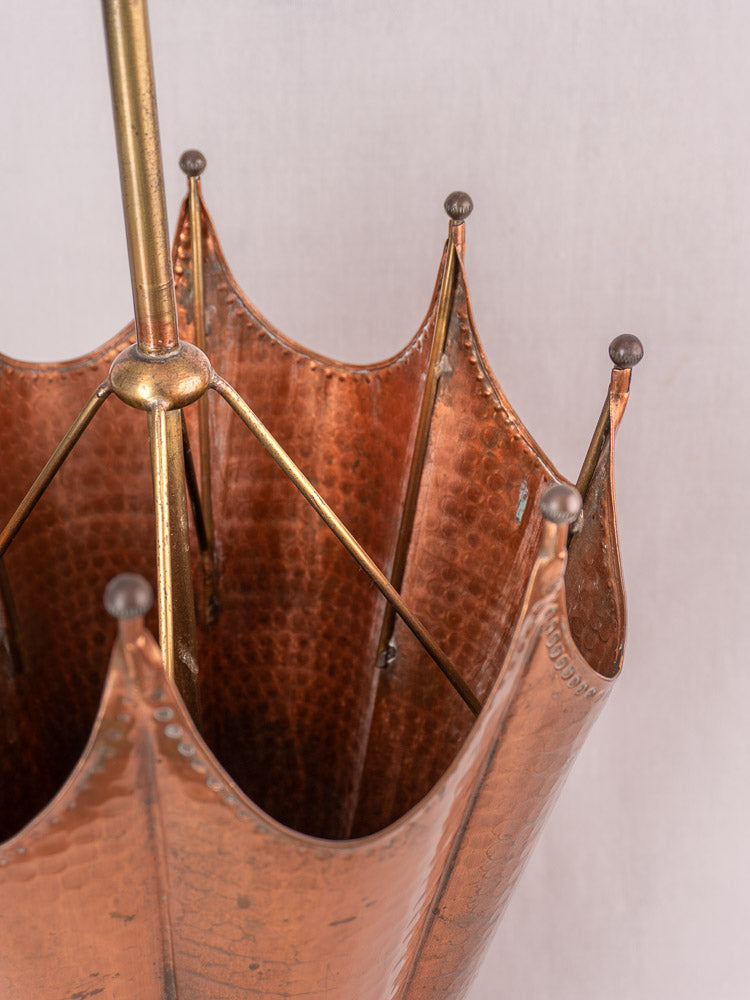 Vintage French hammered copper umbrella stand with brass accents and pointed finials, empty on light background.