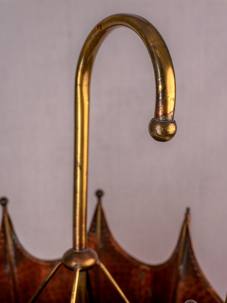 Curved brass handle of a brown umbrella, elegant French metalwork style, on light background.