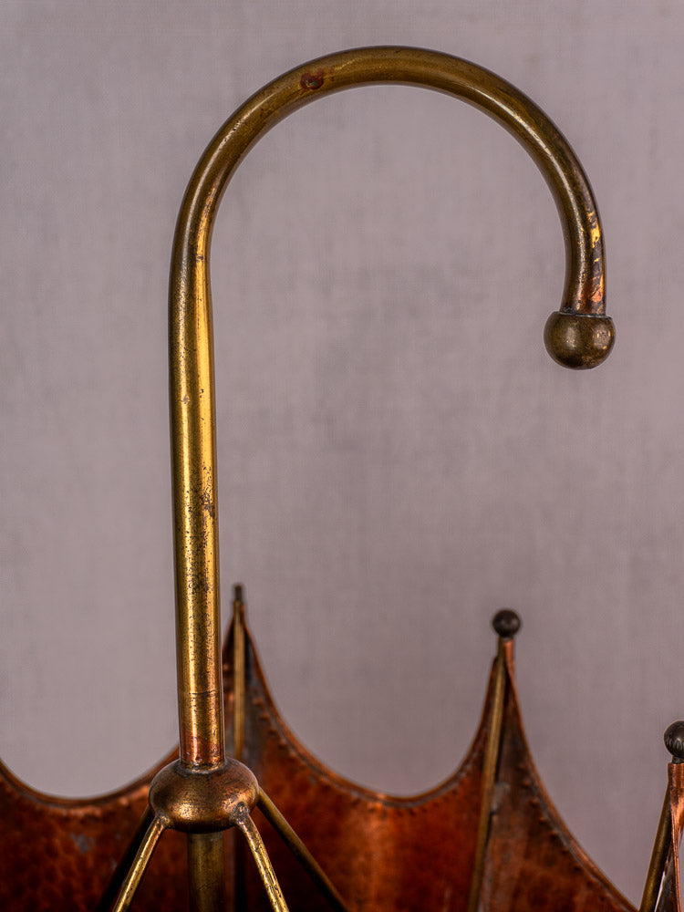 Vintage French umbrella stand in hammered copper and brass with curved handle, plain light background.