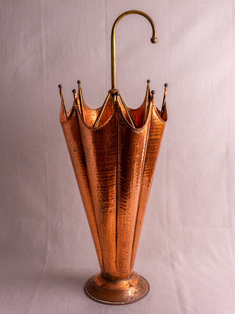 Mid-century French umbrella stand in hammered copper with brass handle and scalloped rim on light background.