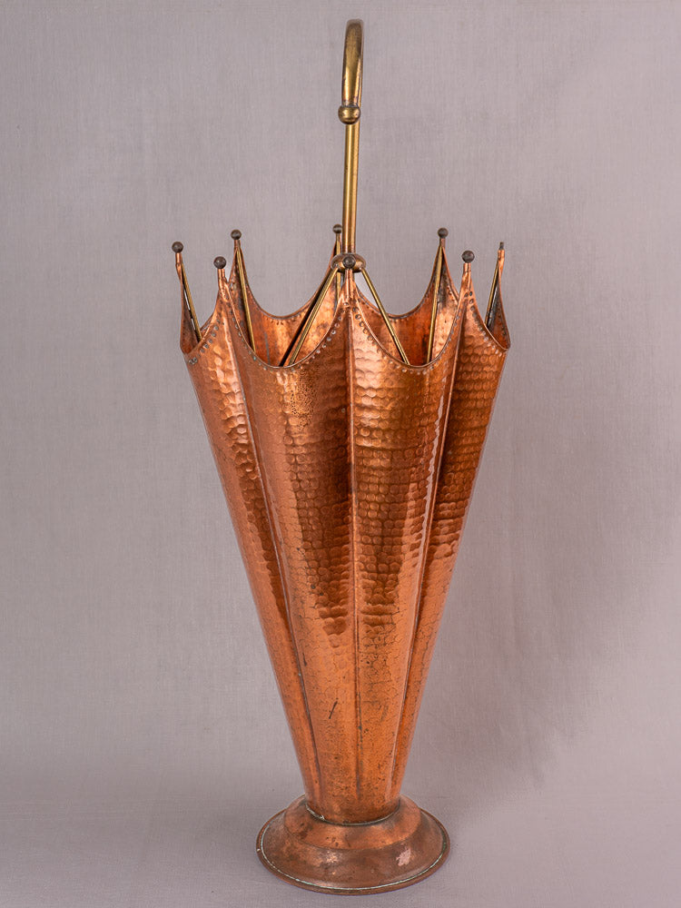 Vintage French hammered copper umbrella stand with crown-shaped top and brass handle on plain background.