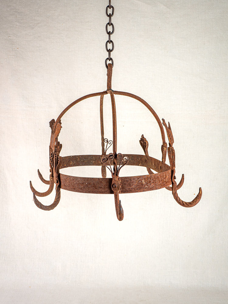 Vintage French wrought iron pot rack with rooster motif, ornate metalwork, six hooks, plain background.
