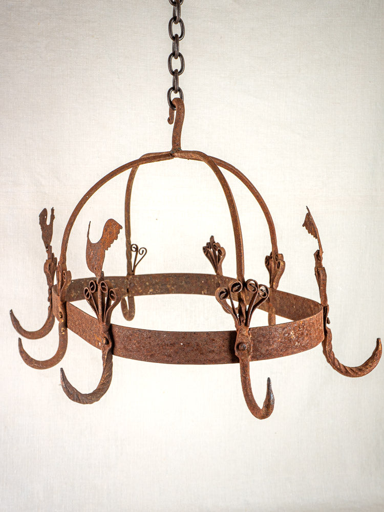 Vintage French wrought iron pot rack with rooster motif, curled accents, and weathered finish hanging from a chain.