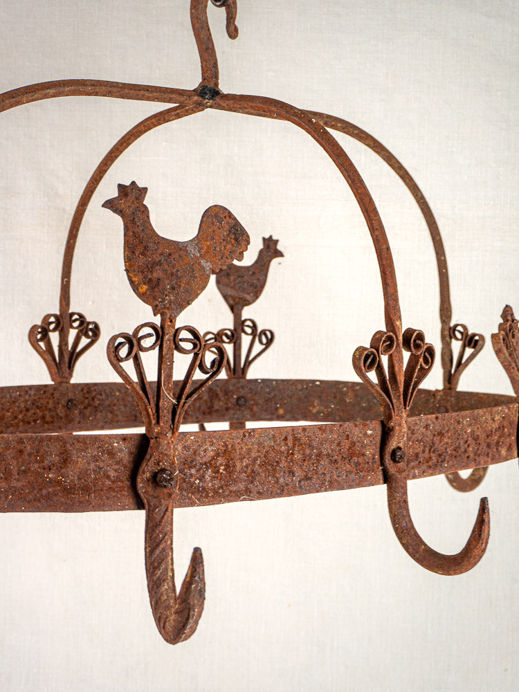 Vintage French wrought iron pot rack with rooster motifs and sturdy hooks on a light background.