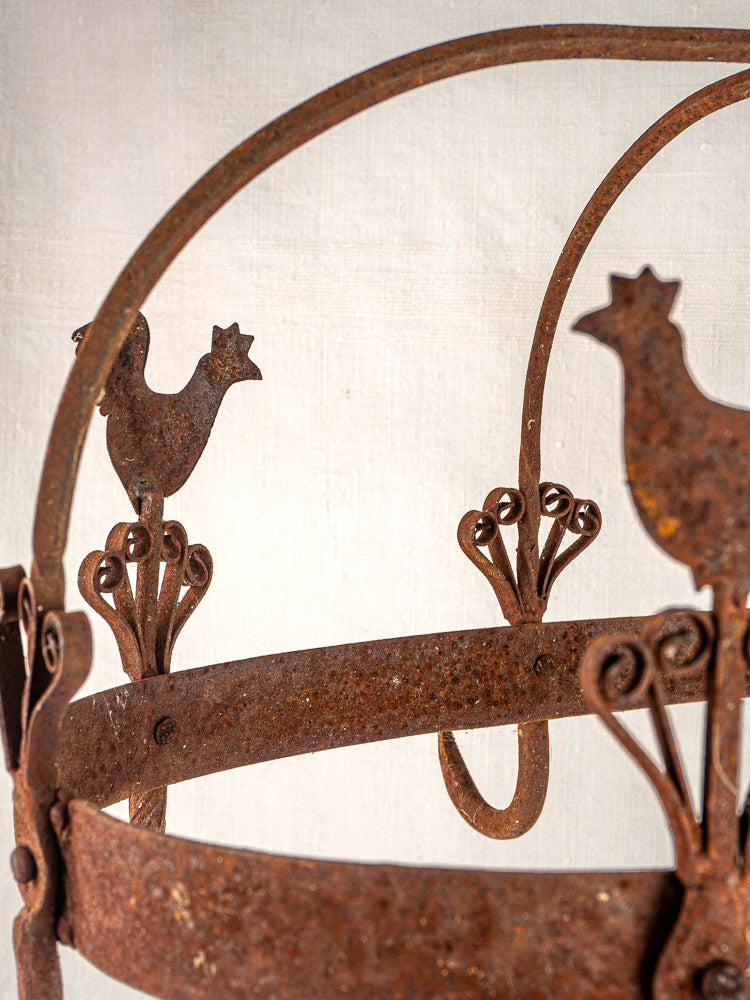 Antique French wrought iron pot rack with rooster motif and curved metalwork, rustic finish.