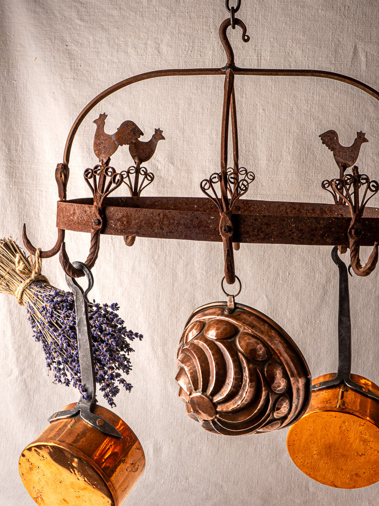 French wrought iron pot rack with rooster motif, displaying copper pots and mold, dried lavender.