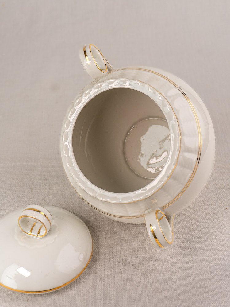 Bernardaud white Limoges porcelain sugar bowl with gold-accented lid on light fabric surface.