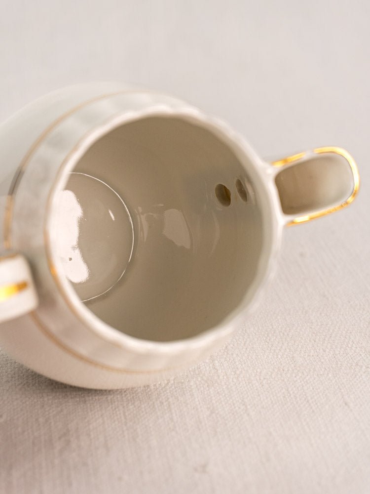 Antique French Limoges white porcelain tea cup with gold-accented handles on a light textured surface.