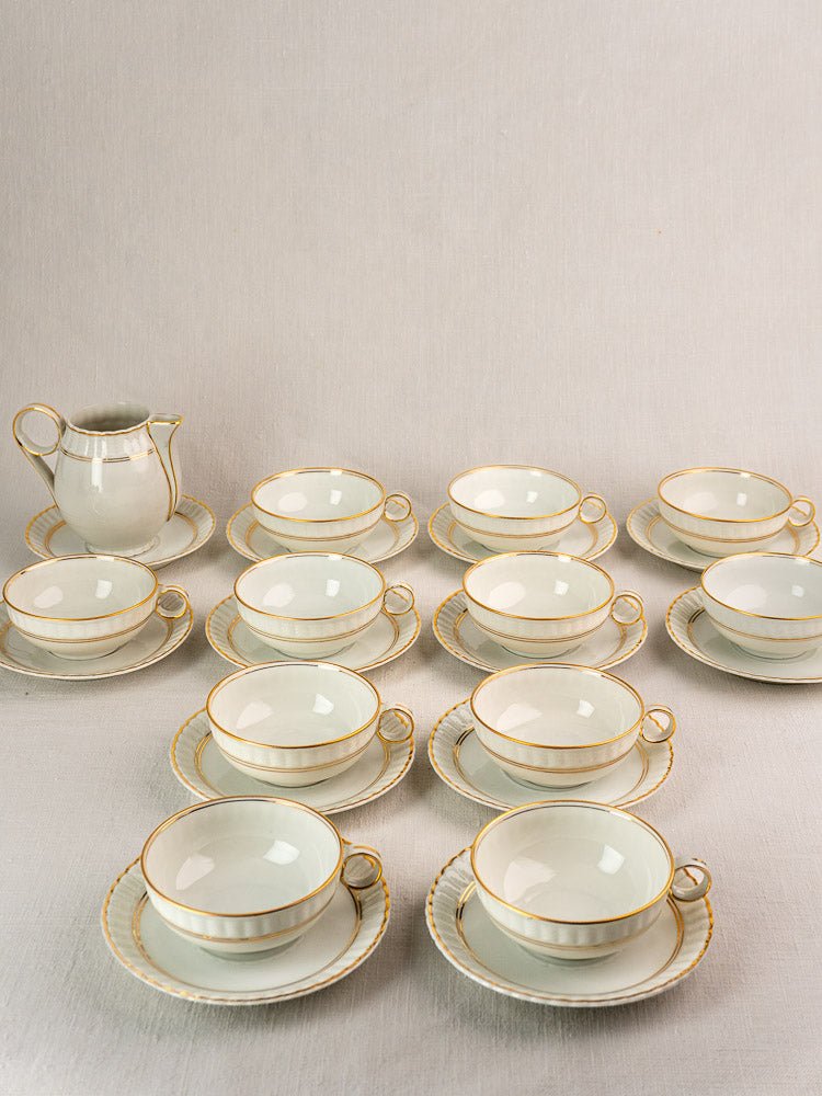 Antique French Limoges Bernardaud porcelain tea set with twelve gold-rimmed teacups, saucers, and creamer.
