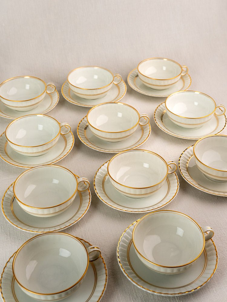 Set of twelve antique French Limoges Bernardaud teacups and saucers with gold rims.