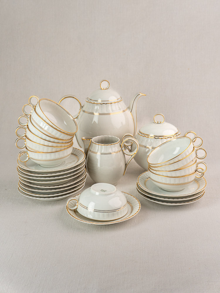Antique French Limoges Bernardaud 26-piece porcelain tea set with gold trim on light surface.