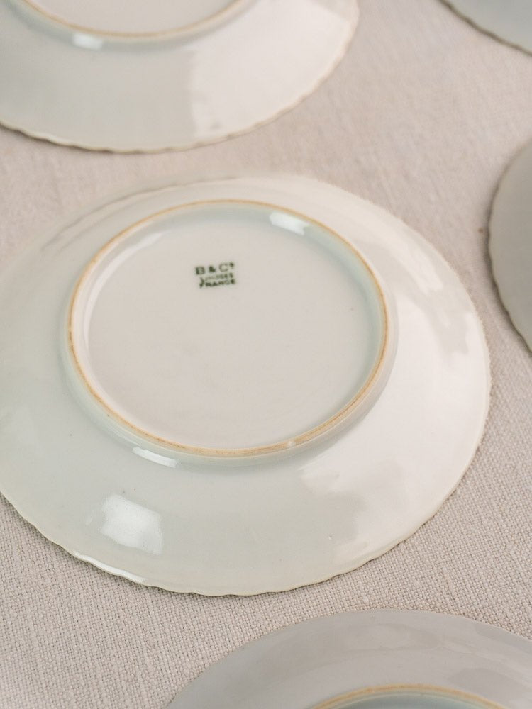 Upside-down white porcelain Limoges plates with D&C France mark on a textured beige background.