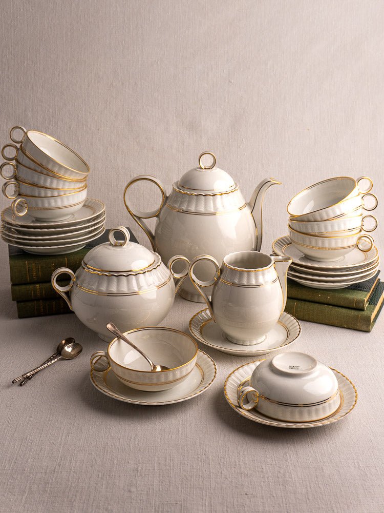 Antique French Limoges Bernardaud 26-piece porcelain tea set with gold trim on stacked books and fabric.