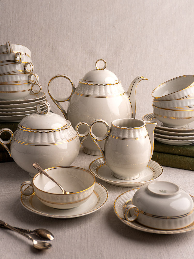 Antique French Limoges Bernardaud 26-piece porcelain tea set with gold trim on light surface.