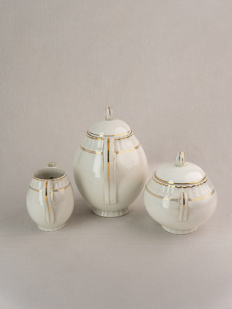Antique French Limoges Bernardaud tea service pieces in white porcelain with gold trim on neutral background.
